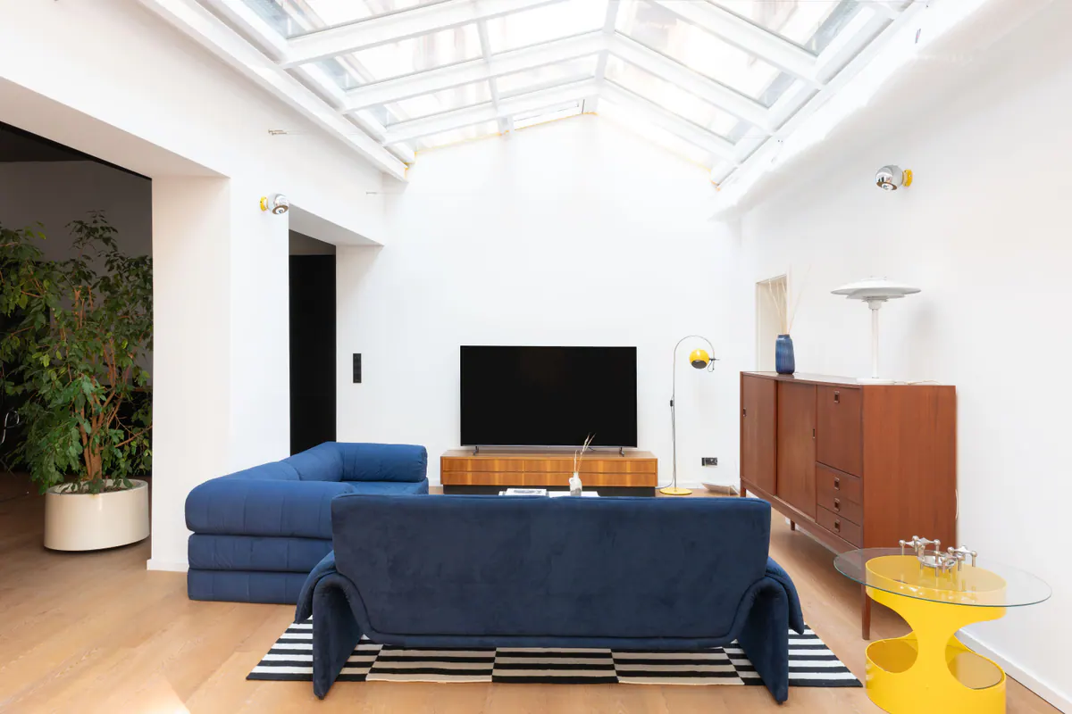 Wohnbereich von Apartment 0.02 mit Oberlicht, tiefblauen Sofas und gelbem Beistelltisch