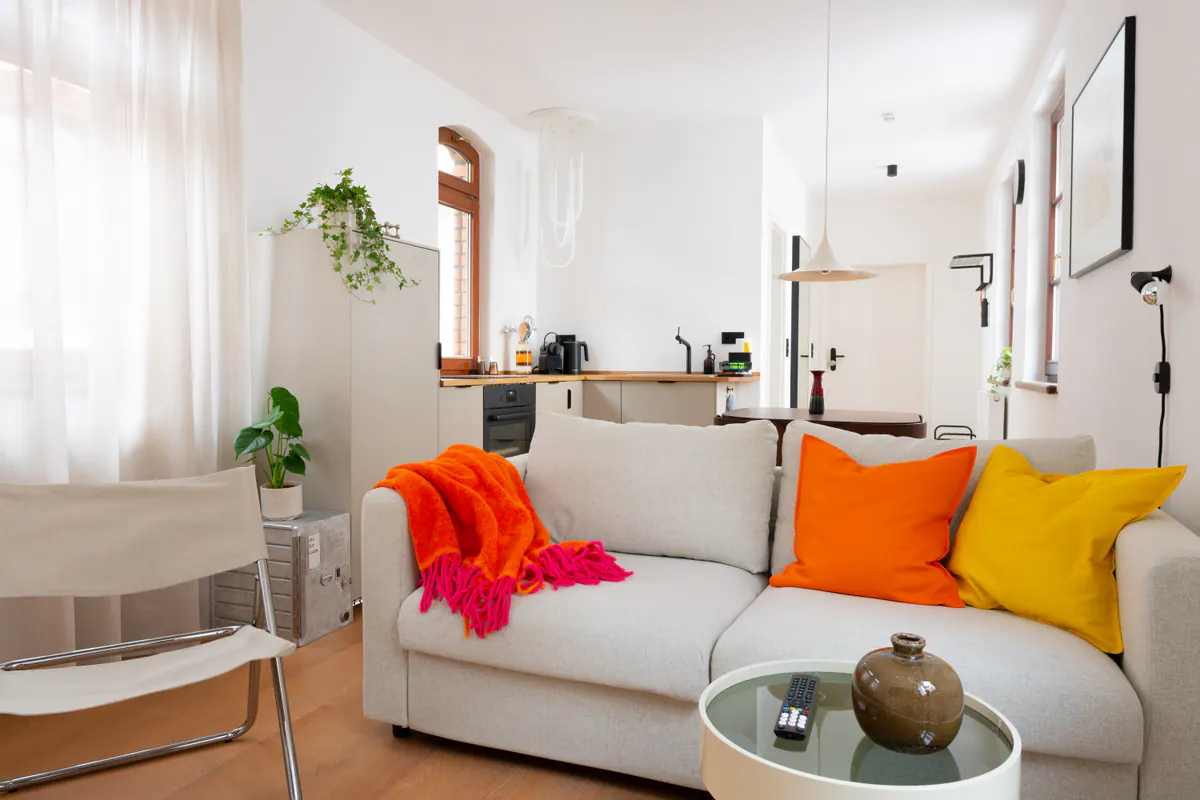 Wohnbereich von Apartment 1.01 mit heller Küche, Sofa und kräftigen Farbakzenten