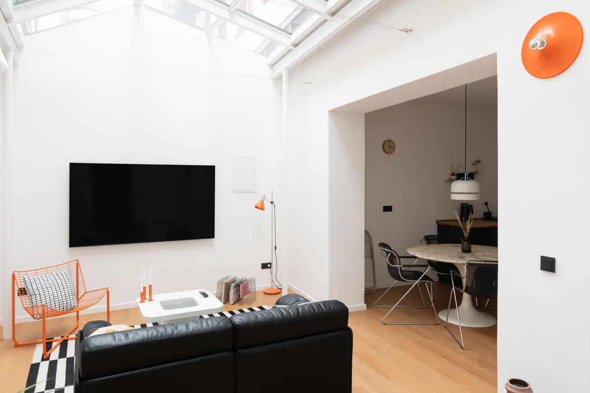 Wohn- und Essbereich von Apartment 0.01 mit Oberlicht, schwarzem Ledersofa und orangefarbenem Sessel