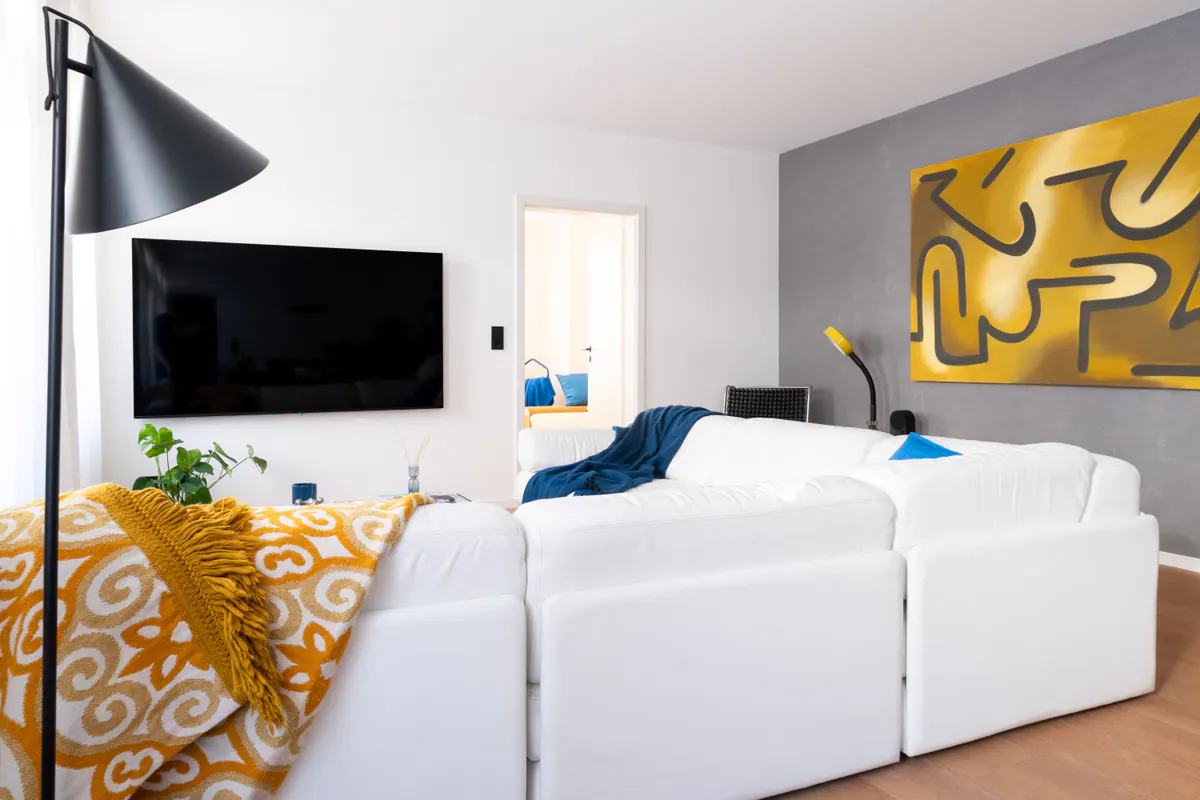 Wohnbereich von Apartment 1.02 mit weißem Sofa, gelbem Kunstwerk und blauen Akzenten